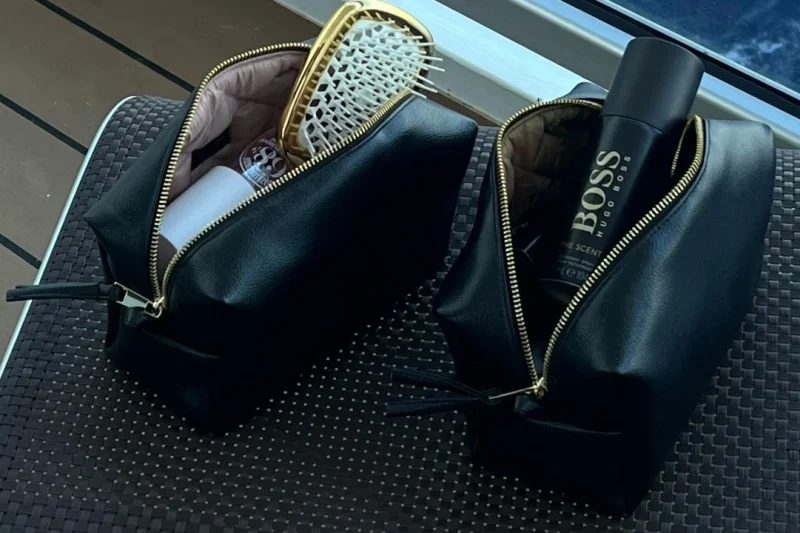 crni-neseser-kozmetika Crne neseser torbice sa kozmetikom i četkom na stolu pored prozora.